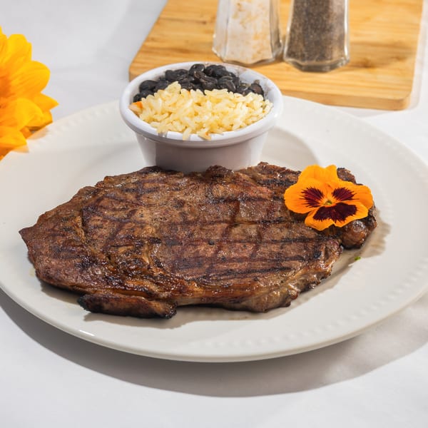 Grilled steak with a side of rice and black beans, garnished with an orange flower.