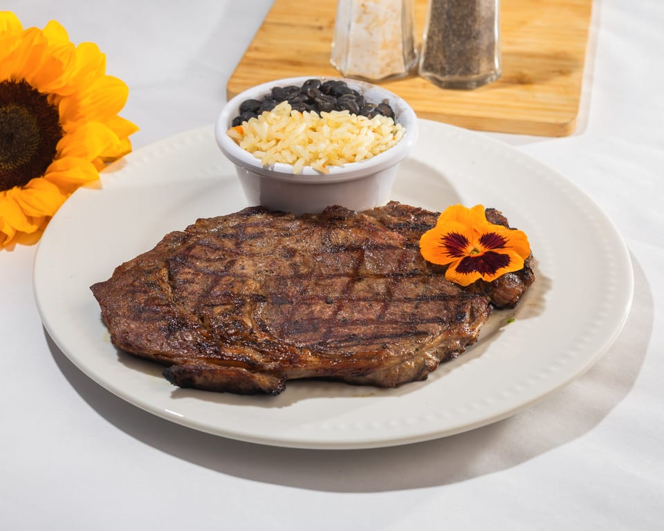 Grilled steak with a side of rice and black beans, garnished with an orange flower.