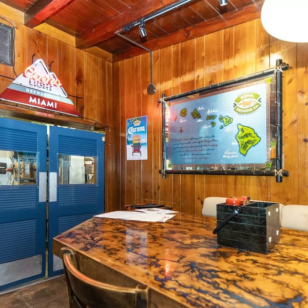 A rustic restaurant interior with wood paneling, a patterned table, and a Kona Brewing Co. map.