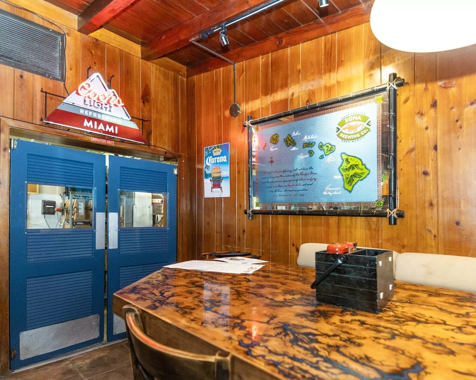 A rustic restaurant interior with wood paneling, a patterned table, and a Kona Brewing Co. map.