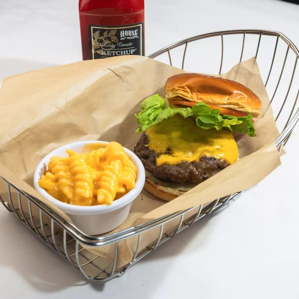 Cheeseburger with lettuce and a side of macaroni and cheese in a wire basket with ketchup.