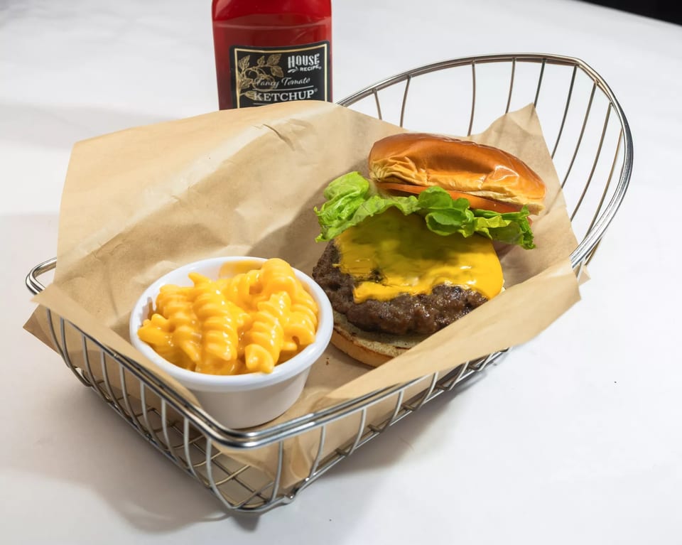 Cheeseburger with lettuce and a side of macaroni and cheese in a wire basket with ketchup.