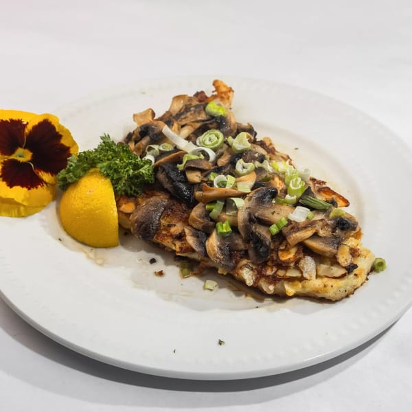 Fish fillet topped with sautéed mushrooms and green onions, garnished with parsley, lemon, and a pansy.