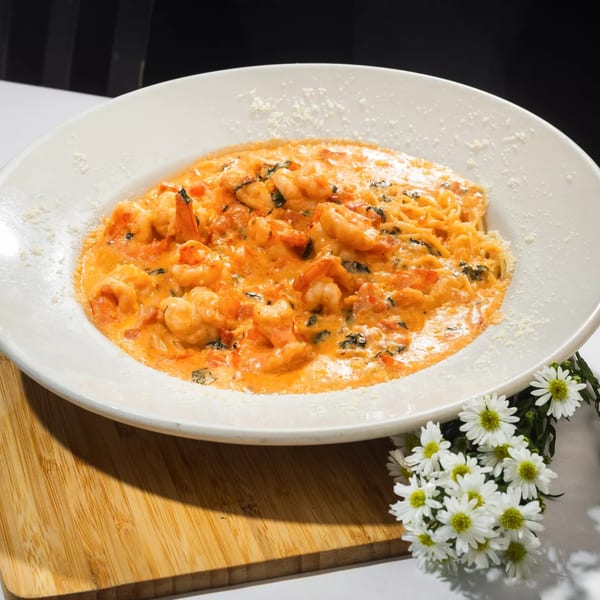 Shrimp pasta in a creamy orange sauce with basil and tomatoes, garnished with parmesan cheese.