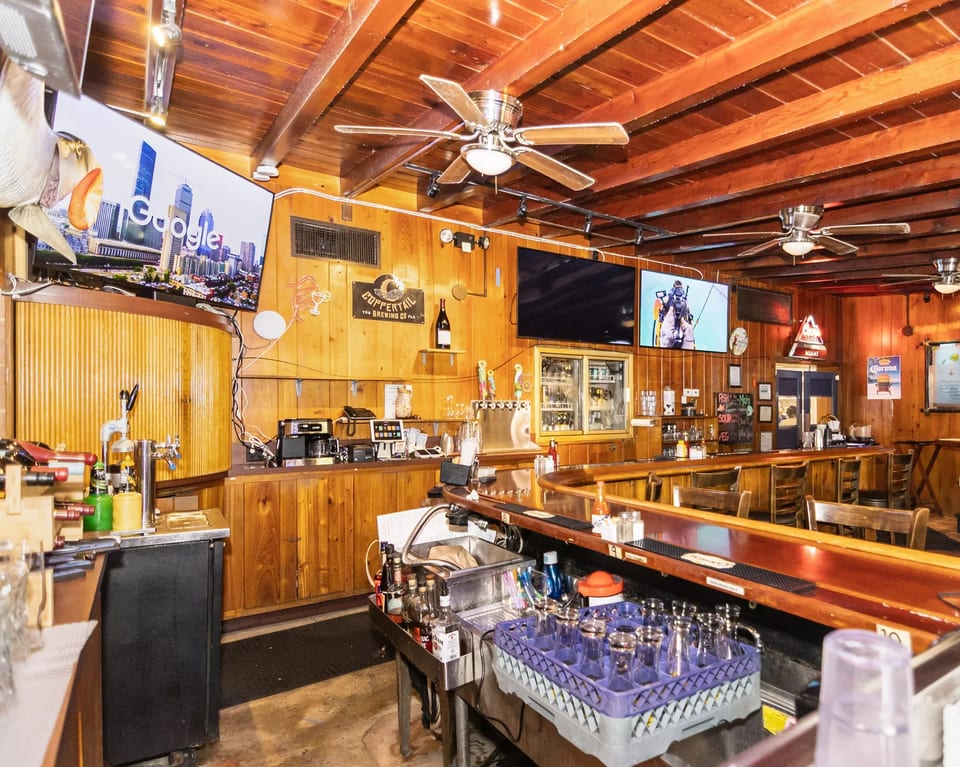 A rustic bar interior with wooden walls and ceiling, multiple TVs, beer taps, and bar stools.