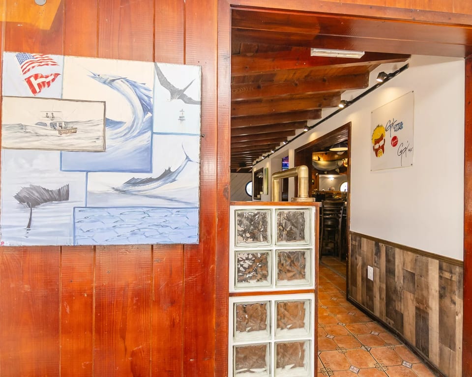 A wooden wall with a fishing-themed painting next to an entryway with glass blocks and a tiled floor.