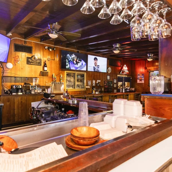 A rustic bar interior with wooden paneling, multiple TVs, beer taps, and hanging glassware.