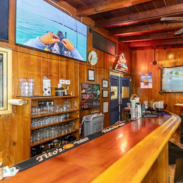 A rustic bar with wooden paneling, a large TV, and a chalkboard menu.