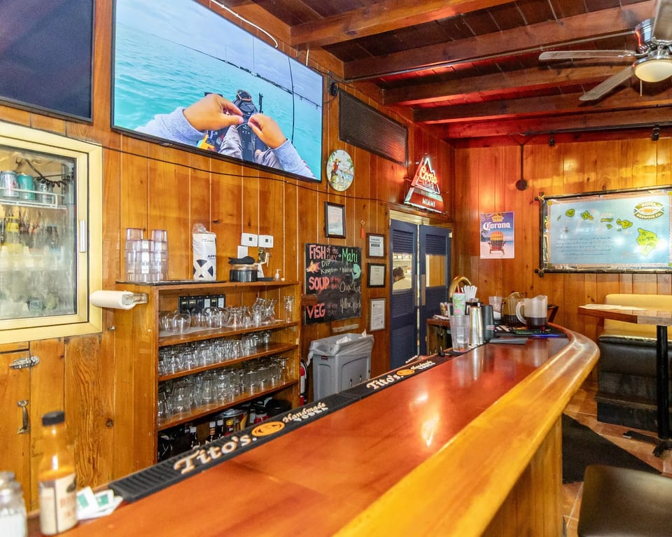 A rustic bar with wooden paneling, a large TV, and a chalkboard menu.