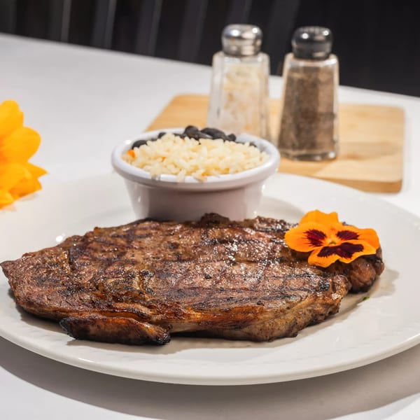 Grilled steak with an edible flower, a side of rice and black beans, and a sunflower.