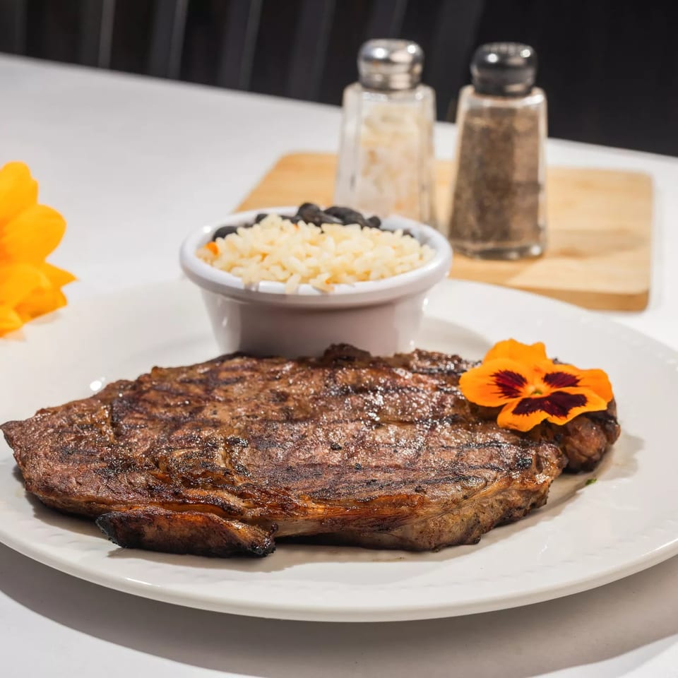 Grilled steak with an edible flower, a side of rice and black beans, and a sunflower.