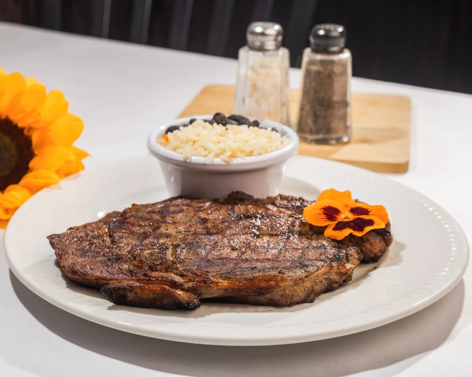 Grilled steak with an edible flower, a side of rice and black beans, and a sunflower.