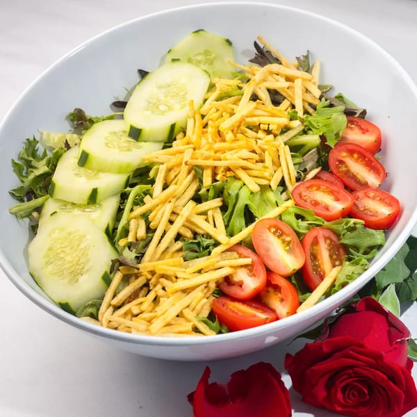 Fresh garden salad with sliced cucumbers, cherry tomatoes, and crispy potato sticks in a white bowl.