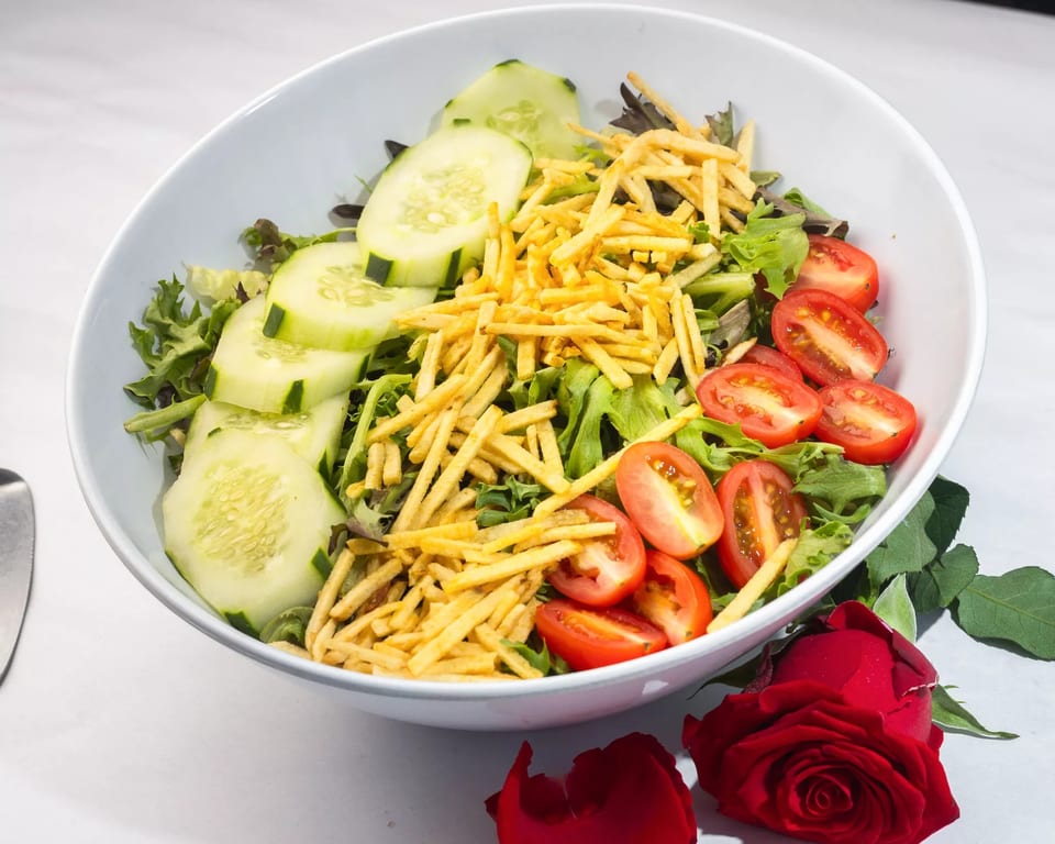 Fresh garden salad with sliced cucumbers, cherry tomatoes, and crispy potato sticks in a white bowl.