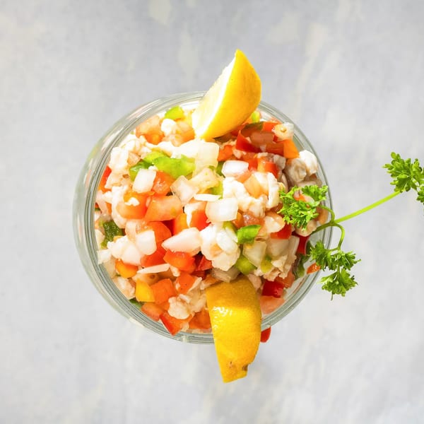 Overhead view of a glass filled with ceviche, garnished with lemon wedges and parsley.