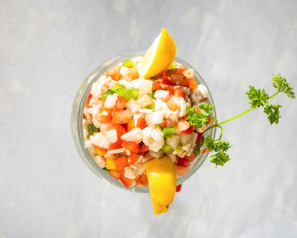 Overhead view of a glass filled with ceviche, garnished with lemon wedges and parsley.
